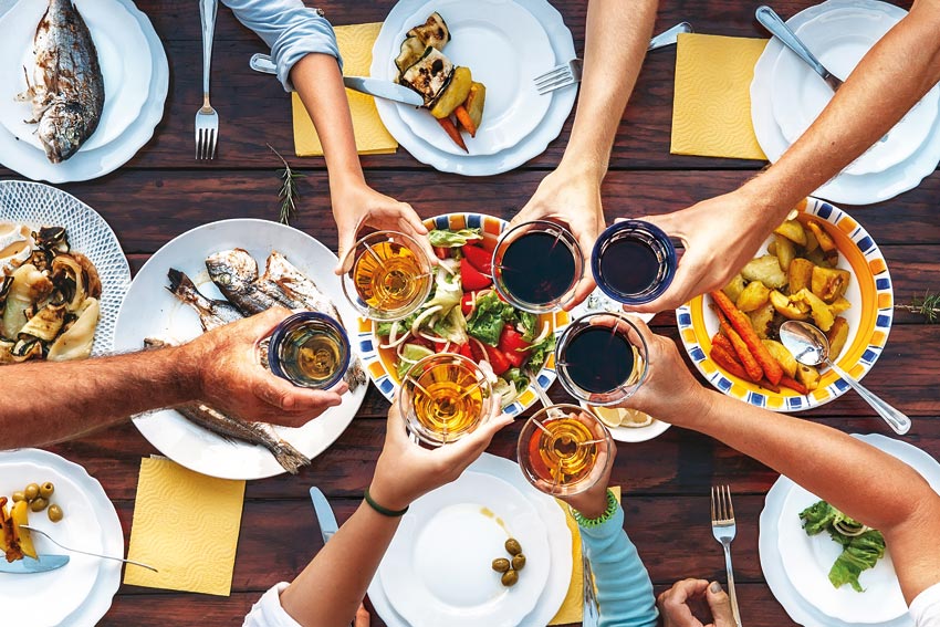 Hände stoßen mit Gläsern Wein an, ein gedeckter Tisch